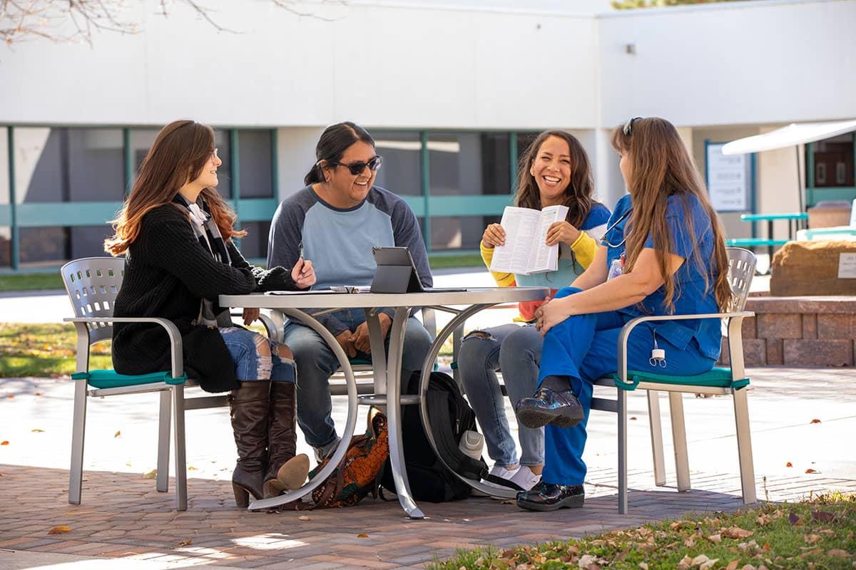 Four San Juan College students sitting at a table outside conversing and smiling.